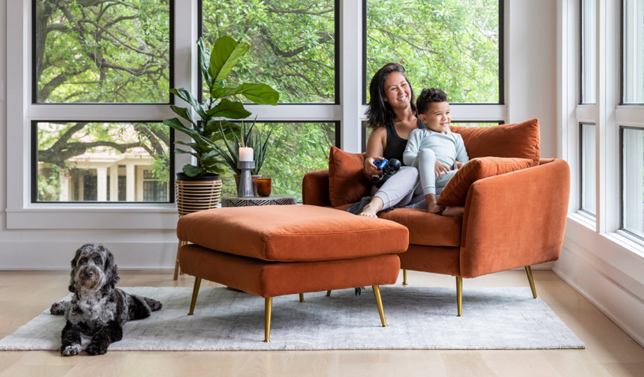 women and child lounging on park armchair and ottoman in rust velvet