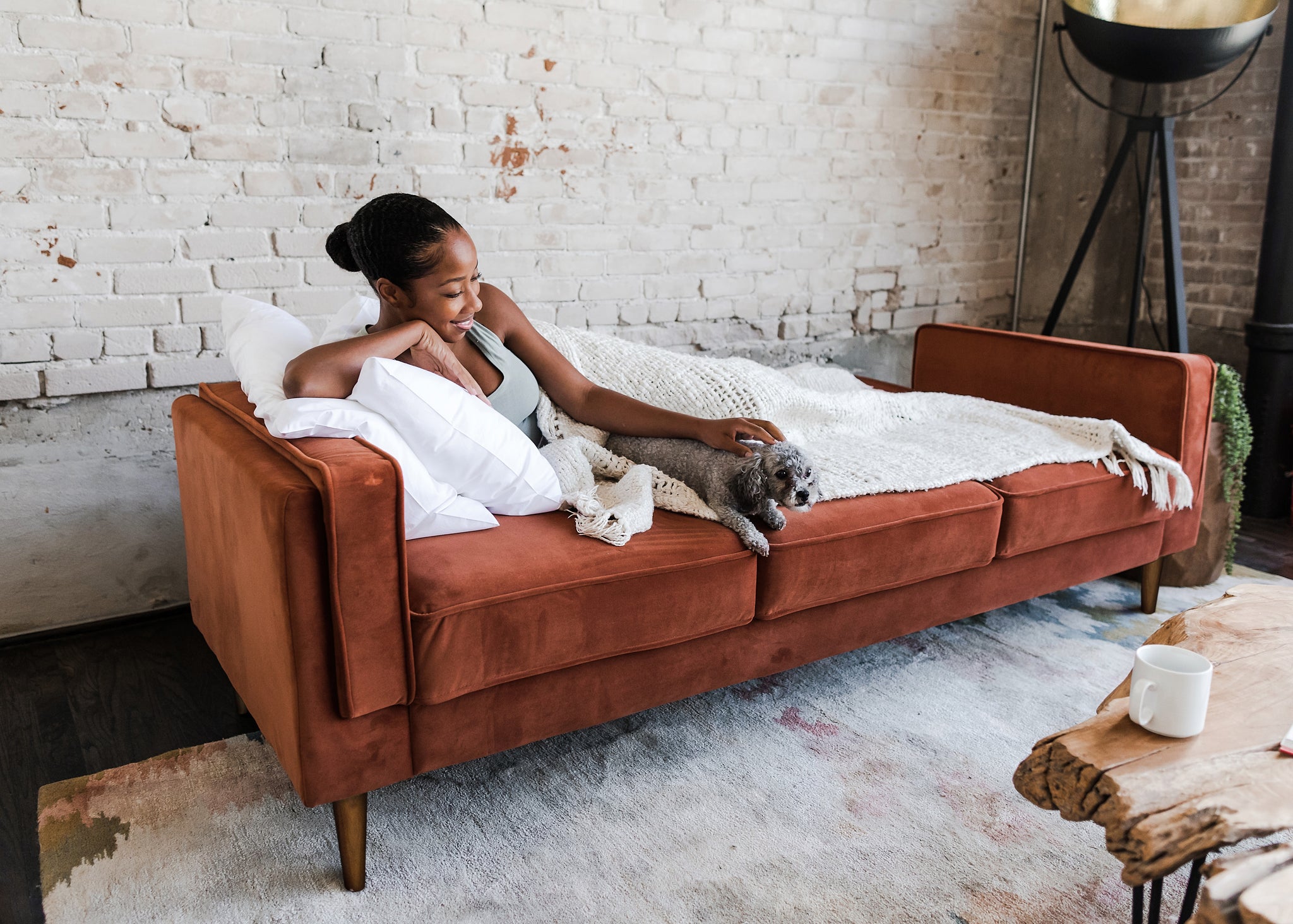 woman lounging with her dog in the albany sofa bed in rust velvet with walnut legs