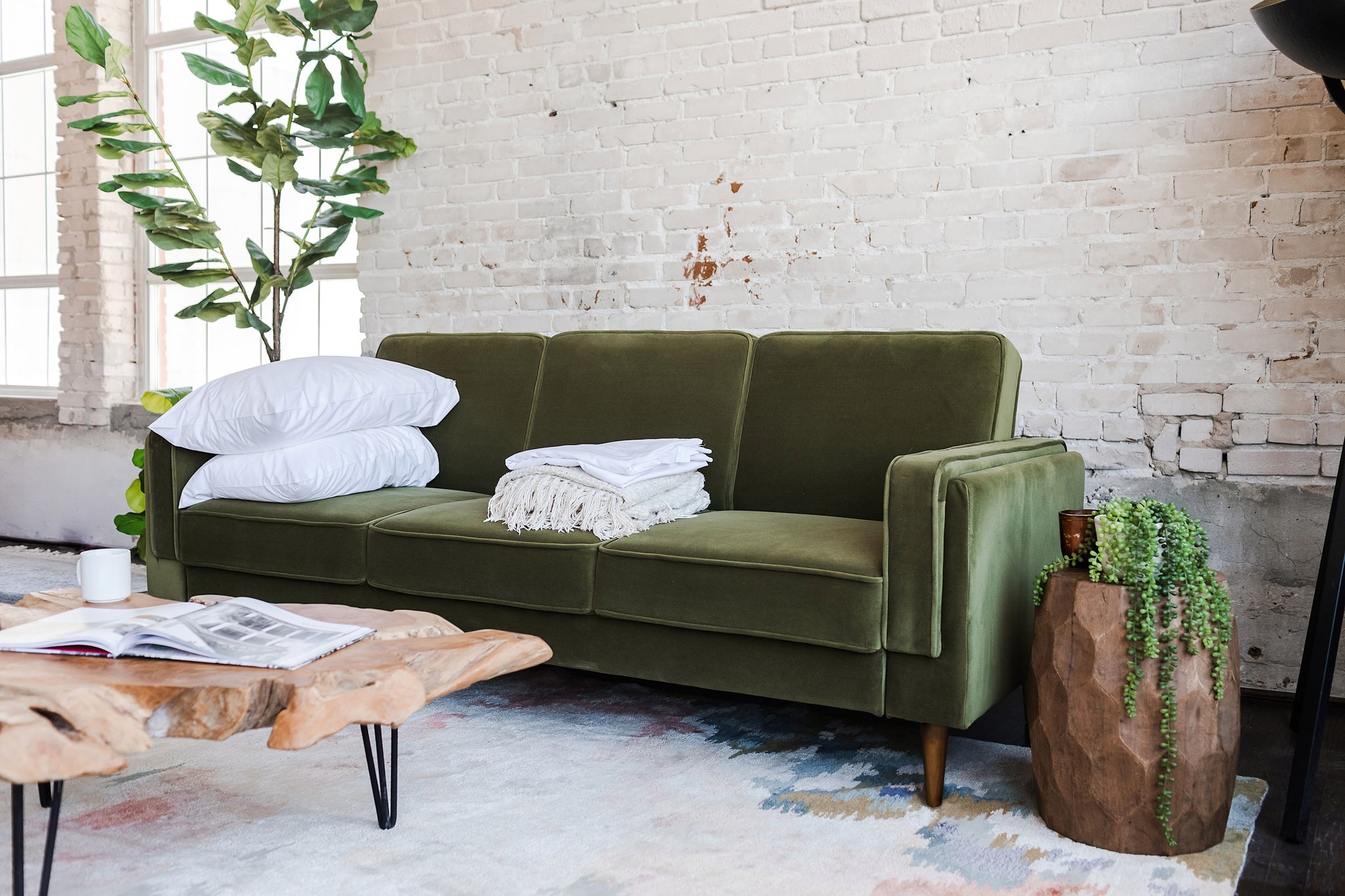 albany sleeper sofa in olive velvet with walnut legs with two pillows and a blanket on top