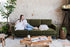 olive velvet walnut | Woman seated in the Albany sleeper sofa in olive velvet with walnut legs