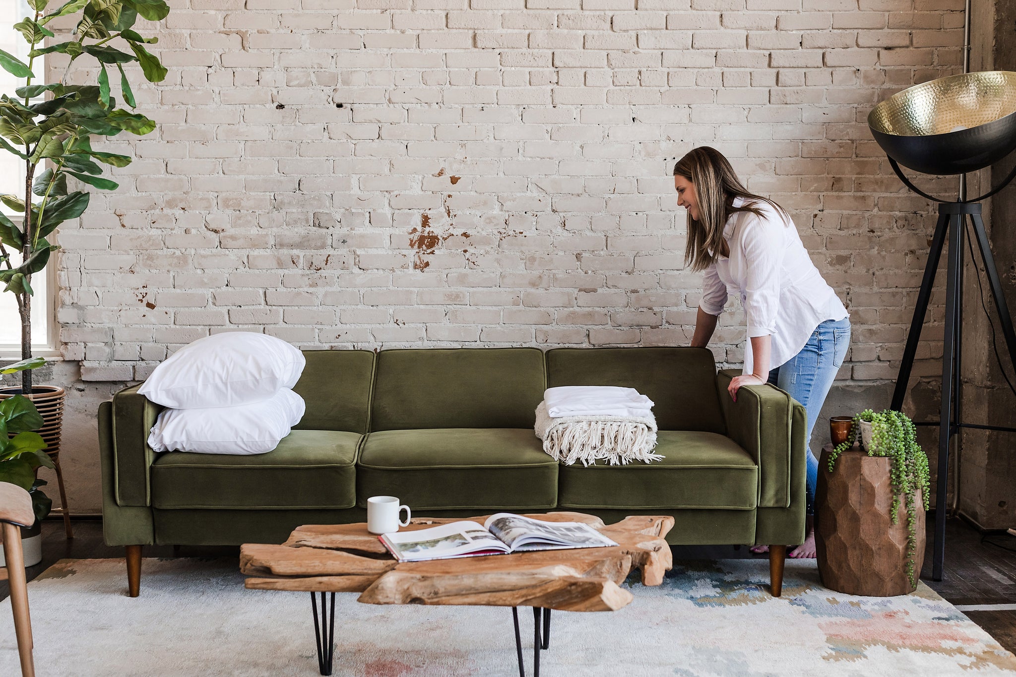 woman opening the albany sleeper sofa in olive velvet with walnut legs
