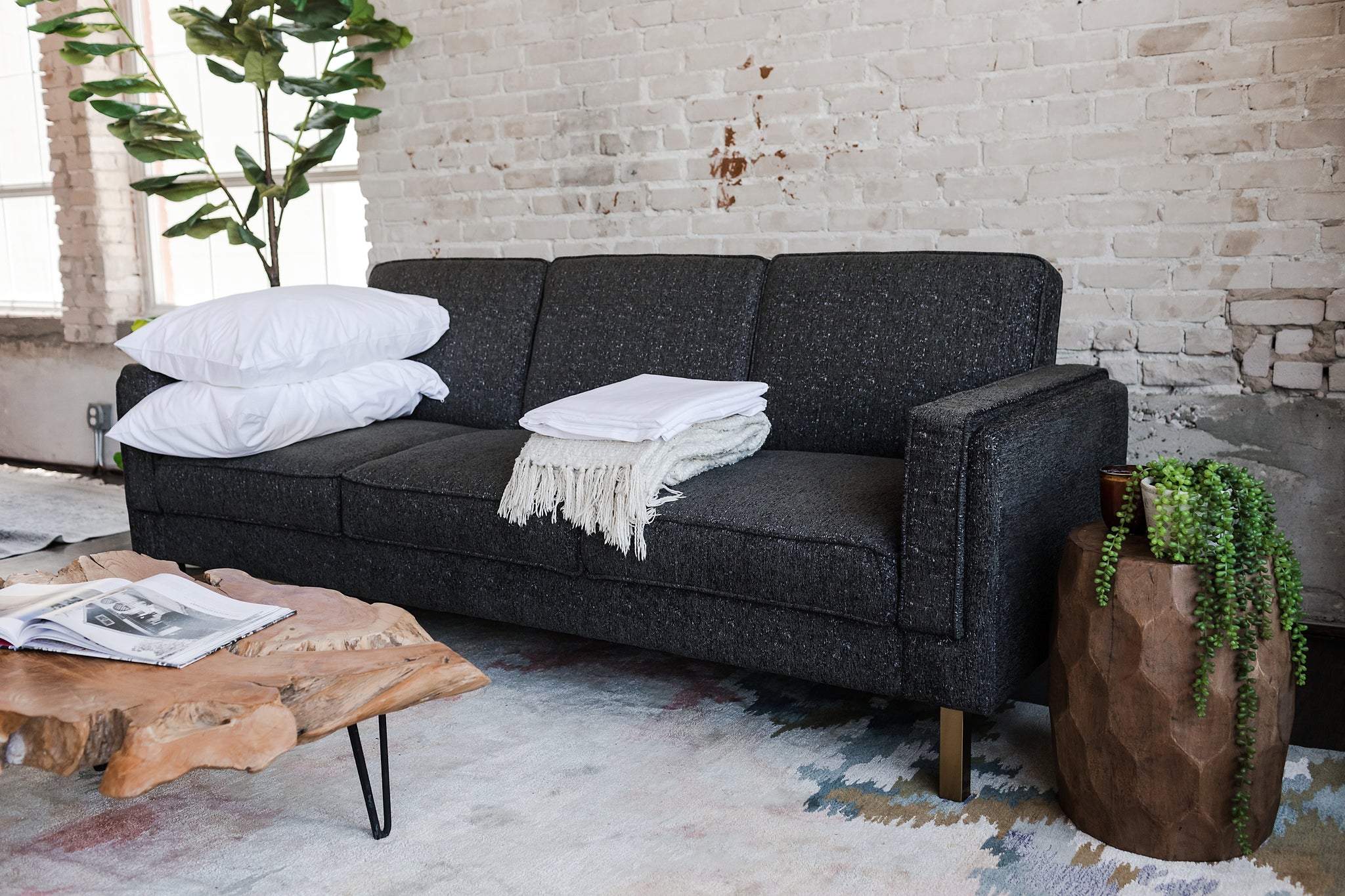 albany sleeper sofa in charcoal with gold legs with two pillows and a blanket on top