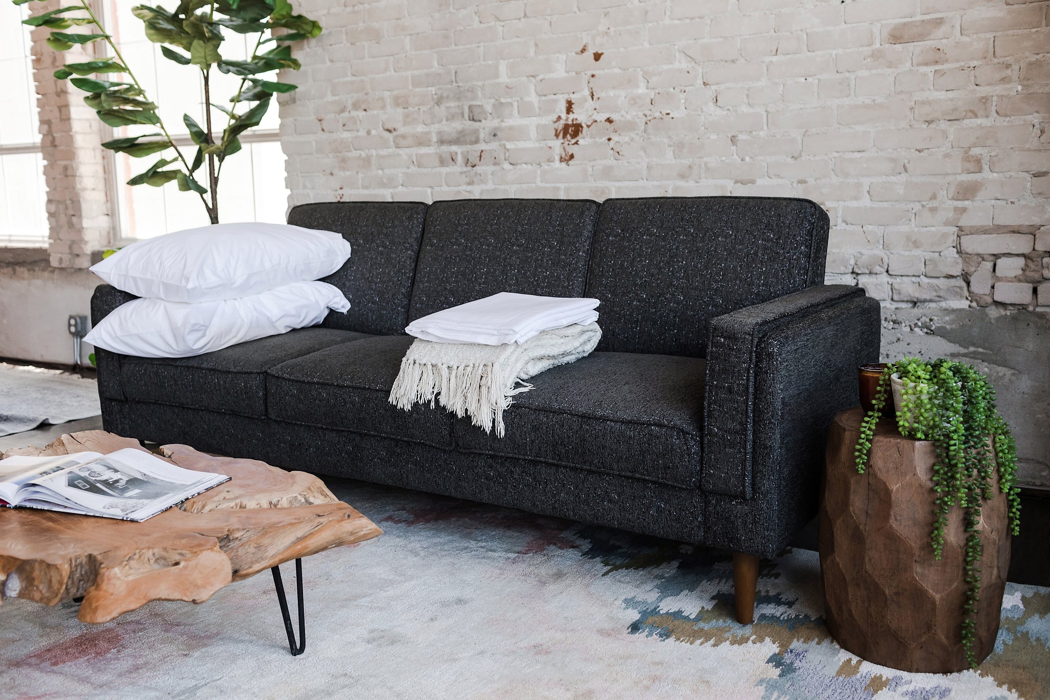 albany sleeper sofa in charcoal with walnut legs with two pillows and a blanket on top