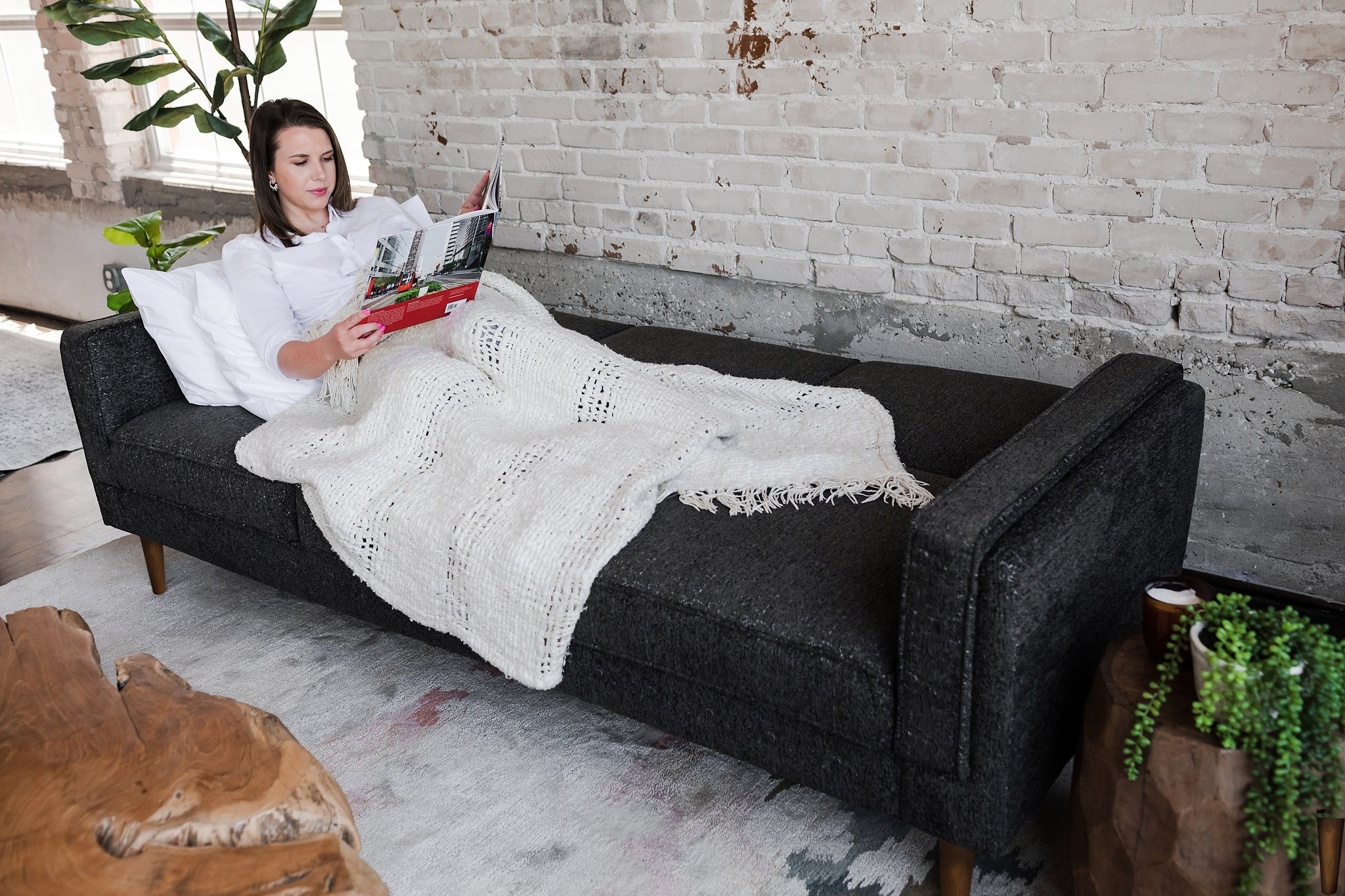 woman lying down in the albany sleeper sofa in charcoal with walnut legs and reading a magazine